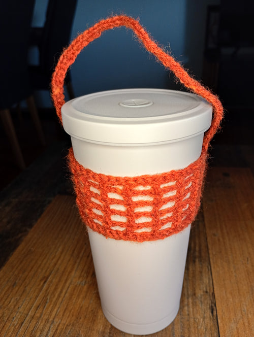 Orangefarbener handgehäkelter Cup Cosy an einem weißen To-go-Becher